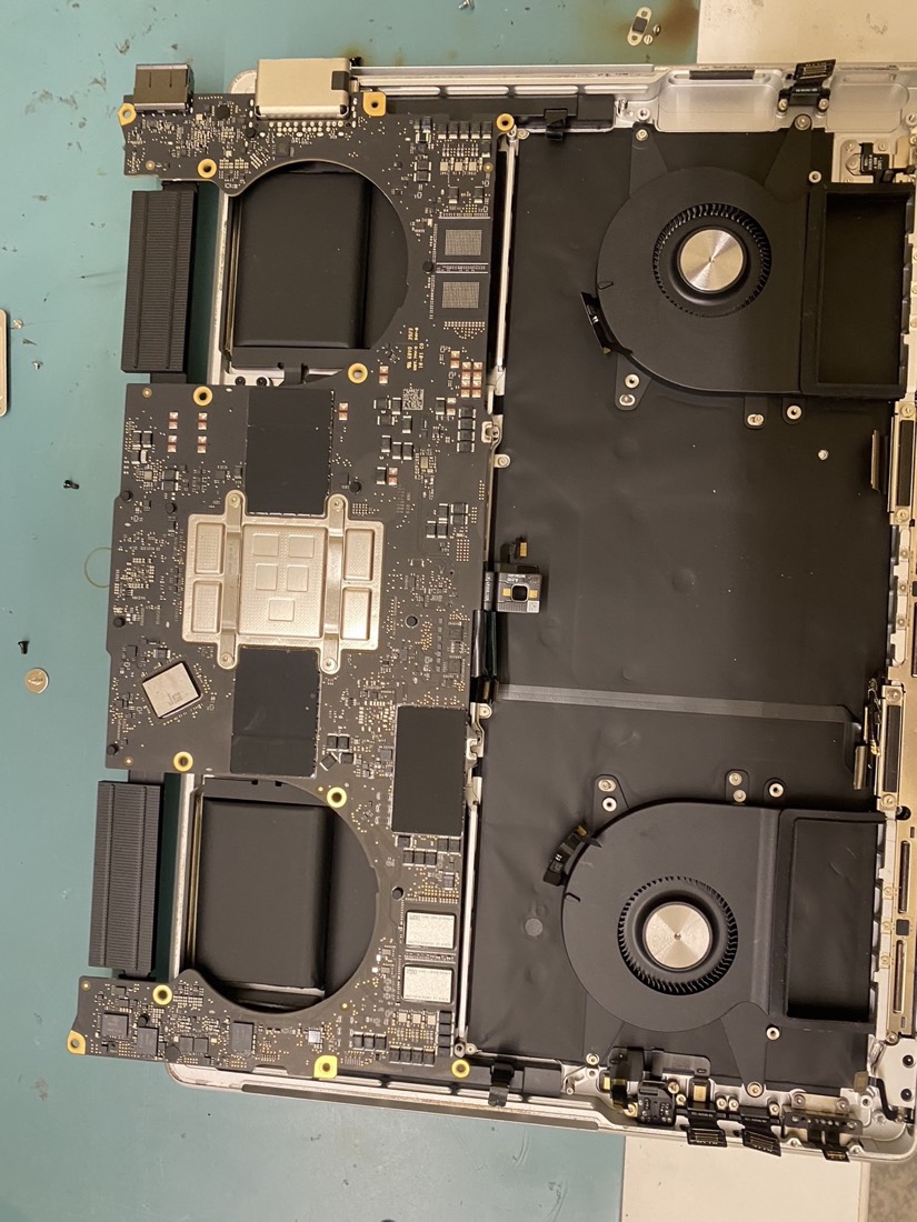 A 14-inch MacBook Pro opened on the bench at MyTechWorld with the logic board and both cooling fans exposed